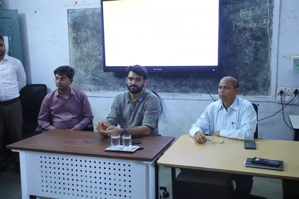 कक्षा में मेजों के पीछे बैठे चार अधिकारी और सामने रखे पानी के गिलास, मोबाइल व रिमोट