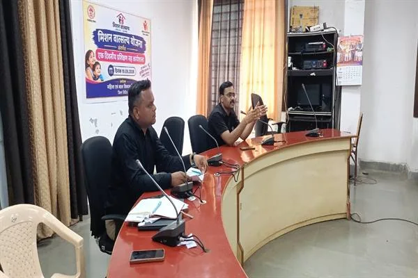 विदिशा कलेक्ट्रेट के सभाकक्ष में मेज पर माइक्रोफोन के सामने बैठे दो प्रशिक्षक, पीछे मिशन वात्सल्य का पोस्टर