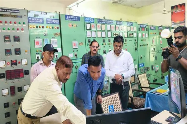हरे नियंत्रण पैनलों वाले विद्युत सब स्टेशन के कक्ष में अधिकारी कंप्यूटर स्क्रीन देखते हुए