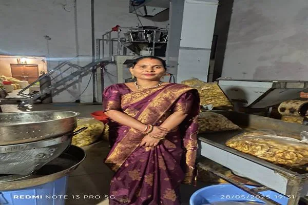बैंगनी साड़ी पहनी एक महिला खाद्य प्रसंस्करण मशीनों और तैयार खाद्य सामग्री के बीच खड़ी हैं