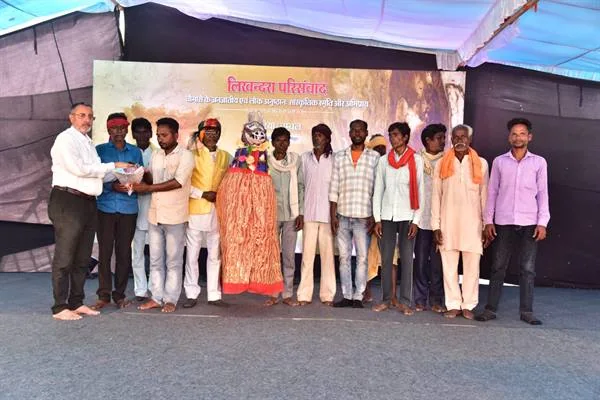 मंच पर पारंपरिक वेशभूषा में लोक कलाकारों के साथ खड़े अतिथि और आयोजक